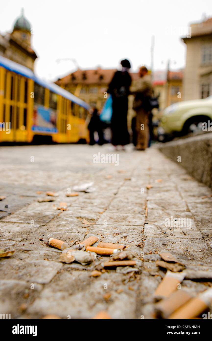 El enfoque selectivo y ver de cerca las colillas de cigarrillos, filtros de esponja sobre el terreno contra la gente borrosa cerca de una estación de autobuses en Praga Foto de stock