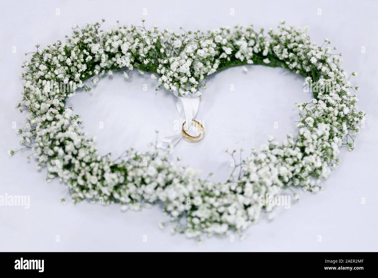 Arreglo de flores blancas en forma de corazón con anillos de boda atados en cinta verde Foto de stock