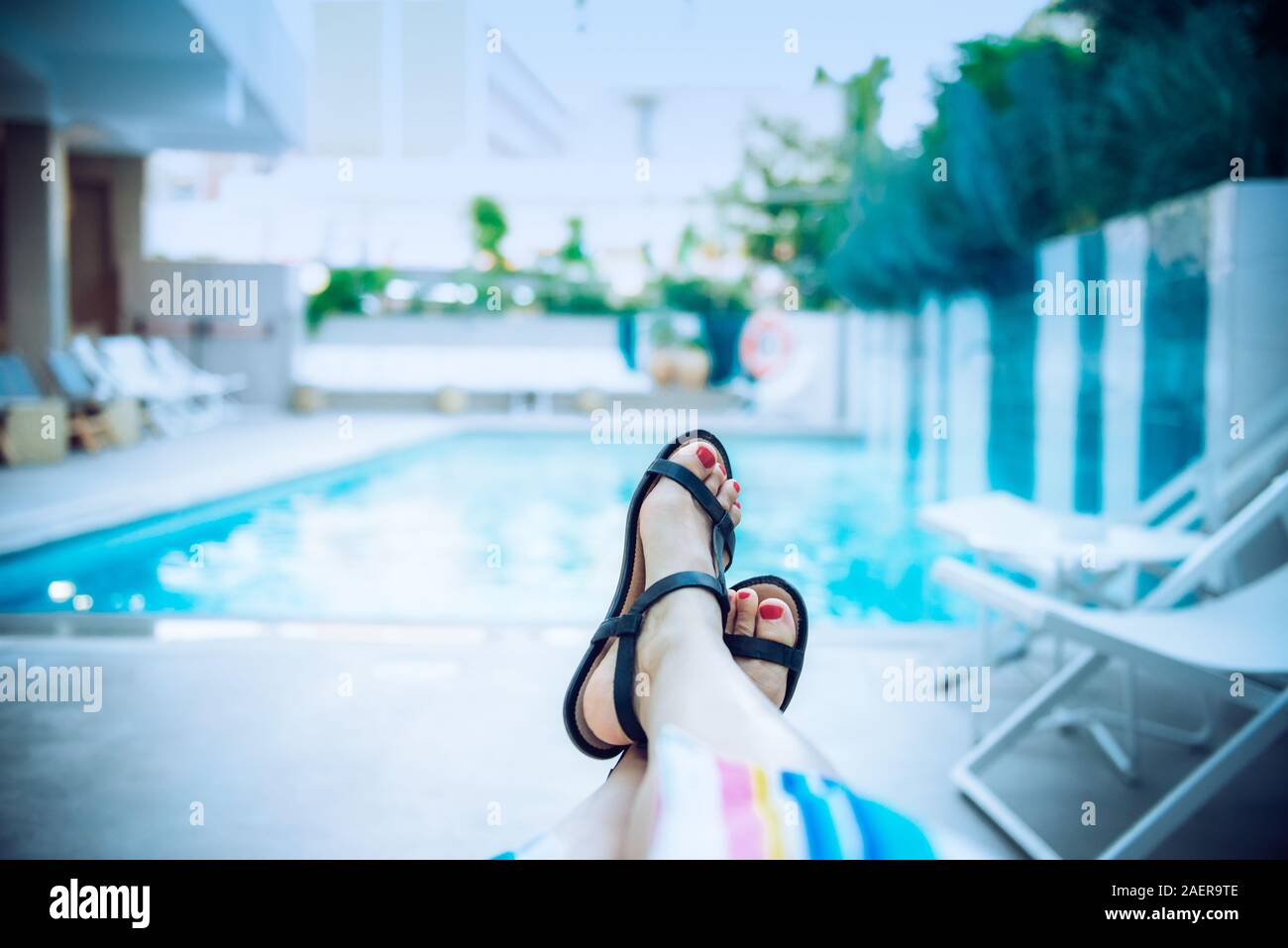 Cerca de los pies femeninos en sandalias relajantes cerca de azul del agua  de la piscina en el hotel por la noche. Calma, lento, la armonía de sus  vacaciones. Concepto de verano