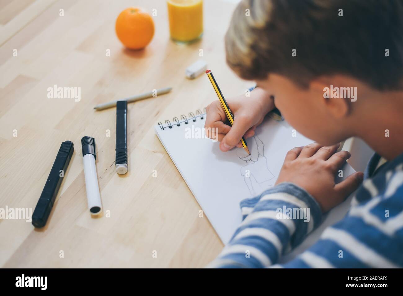 Vista de cerca del estudiante dibujo con lápiz. Boy haciendo los deberes escribiendo en un papel. Kid sostener un lápiz y dibuje un manga en casa. Dibujo adolescente sentado Foto de stock