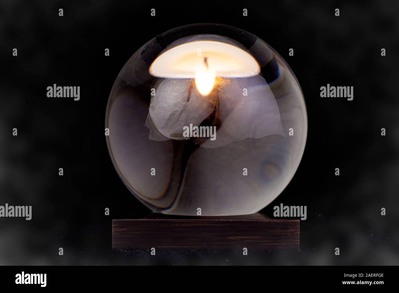Una bola de cristal con una vela reflejada en ella contra un fondo ahumado negro. Foto de stock