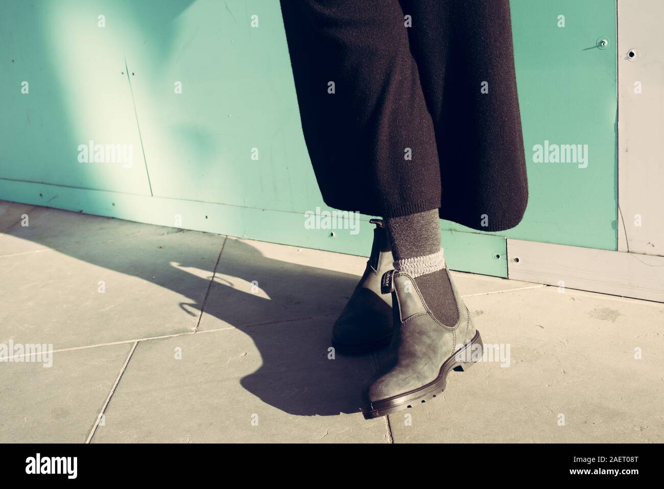 Chelsea botas de cuero negro clásico con suela de goma. Se centran en las piernas de hipster mujer vistiendo de gran tamaño grandes pantalones negros amplia de pierna. Rodado en calle con s Foto de stock