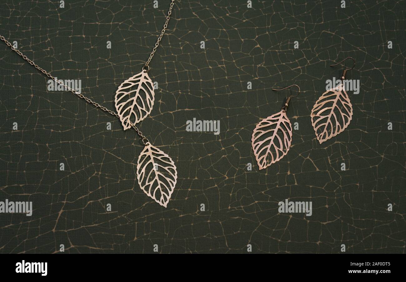 Juego de accesorios de oro inspirado en la naturaleza. Chica Collar y aretes par sobre fondo verde agrietada Foto de stock