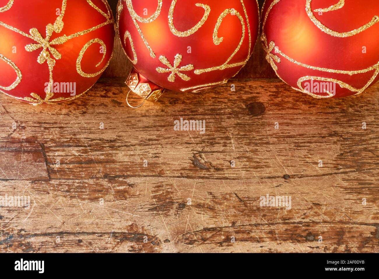 Cerca de las tres bolas de Navidad roja mat con golden swirly decoración en edad oscura mesa de teca con copia espacio para una tarjeta de Navidad o de fondo. Foto de stock