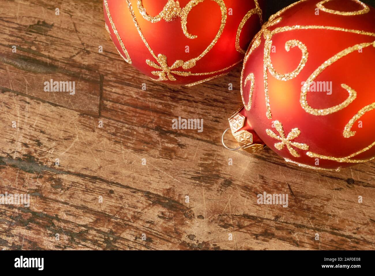 Close-up de dos bolas de Navidad roja mat con golden swirly decoración en edad oscura mesa de teca con copia espacio para un fondo o tarjeta de Navidad Foto de stock