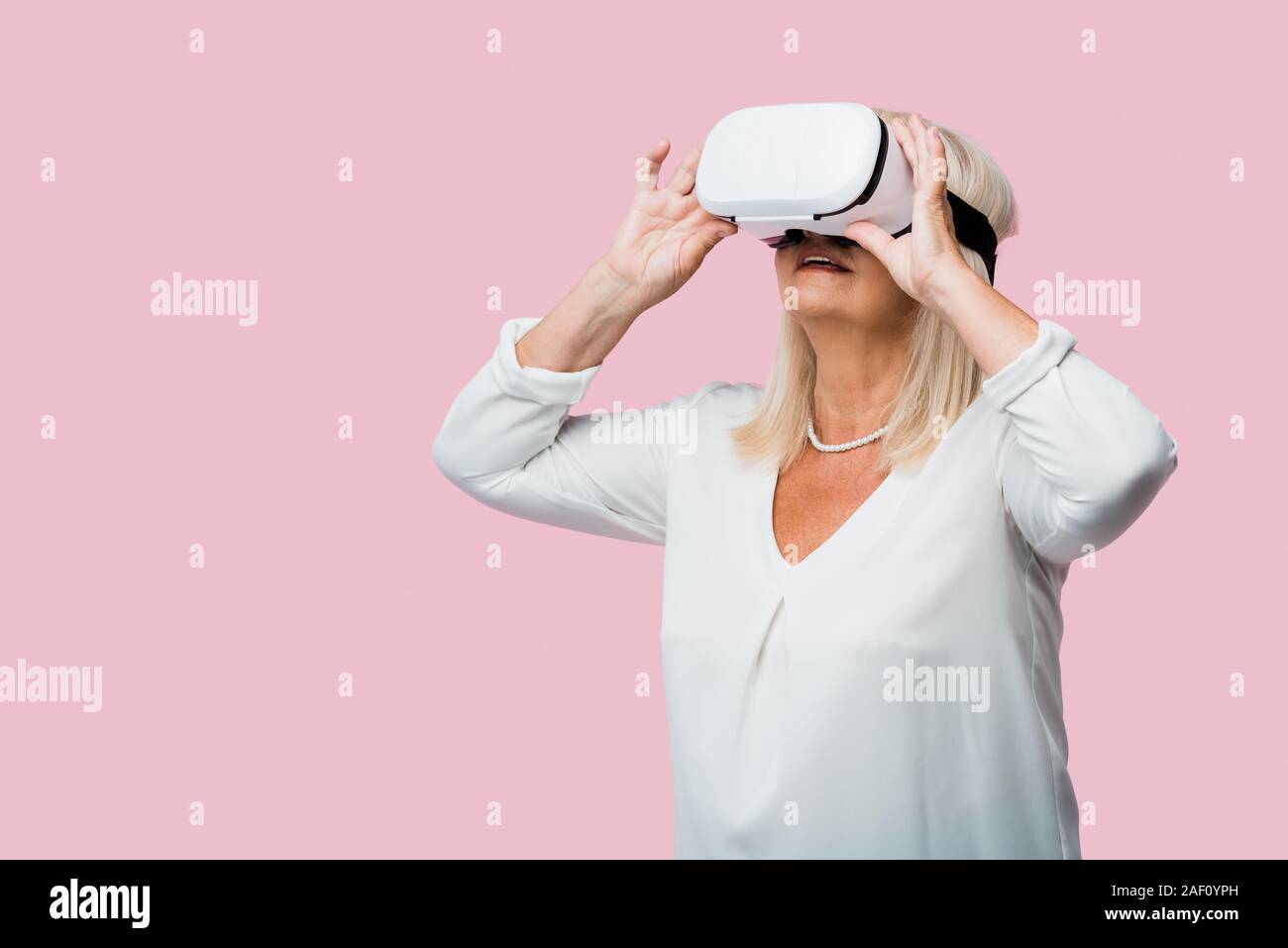 Jubilado mujer vistiendo casco de realidad virtual aislado en rosa Foto de stock
