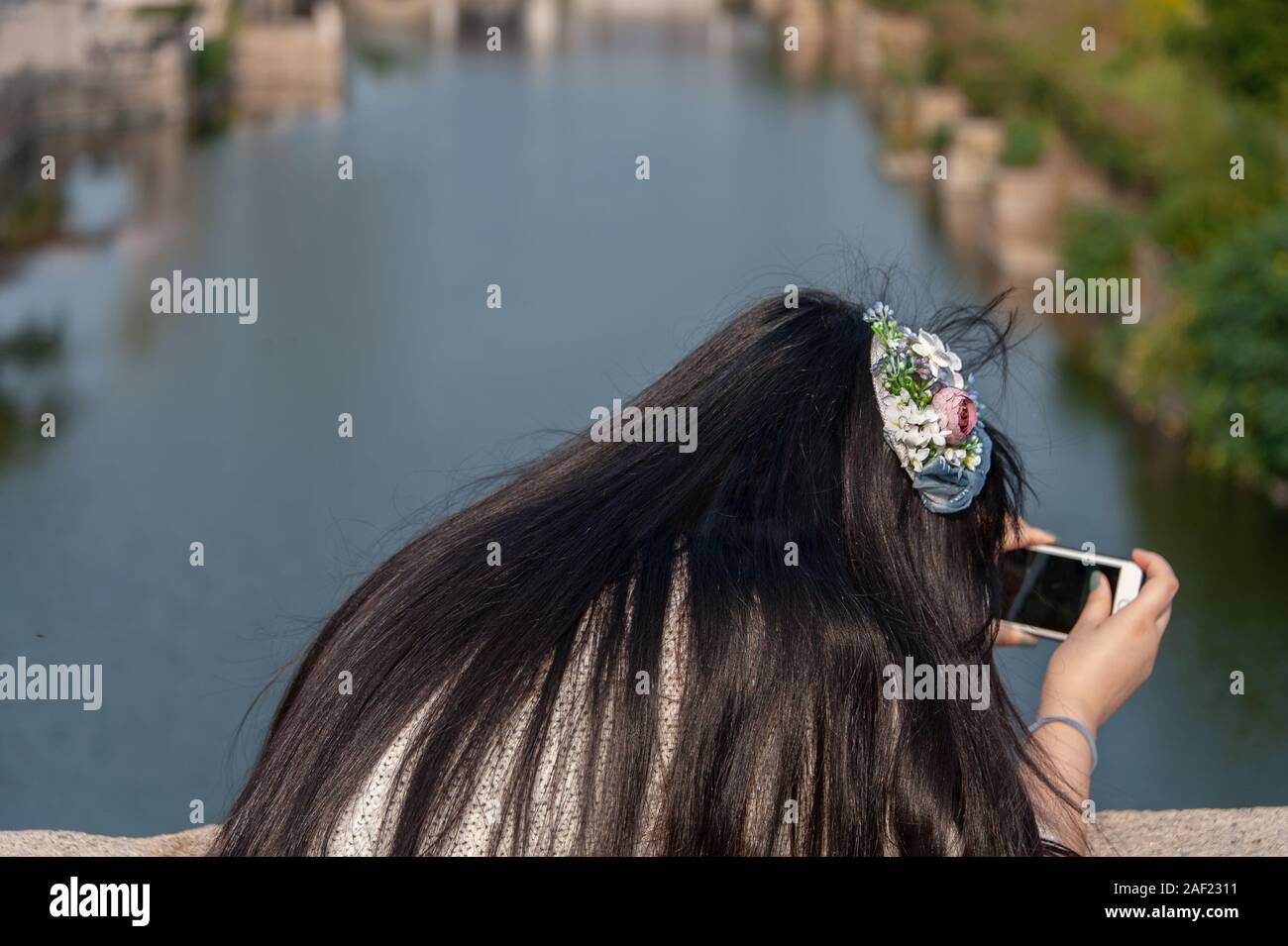 Huishan Ciudad antigua niña china con su espalda a la cámara tomar fotografías con un teléfono celular contra un fondo de agua borrosa. Foto de stock