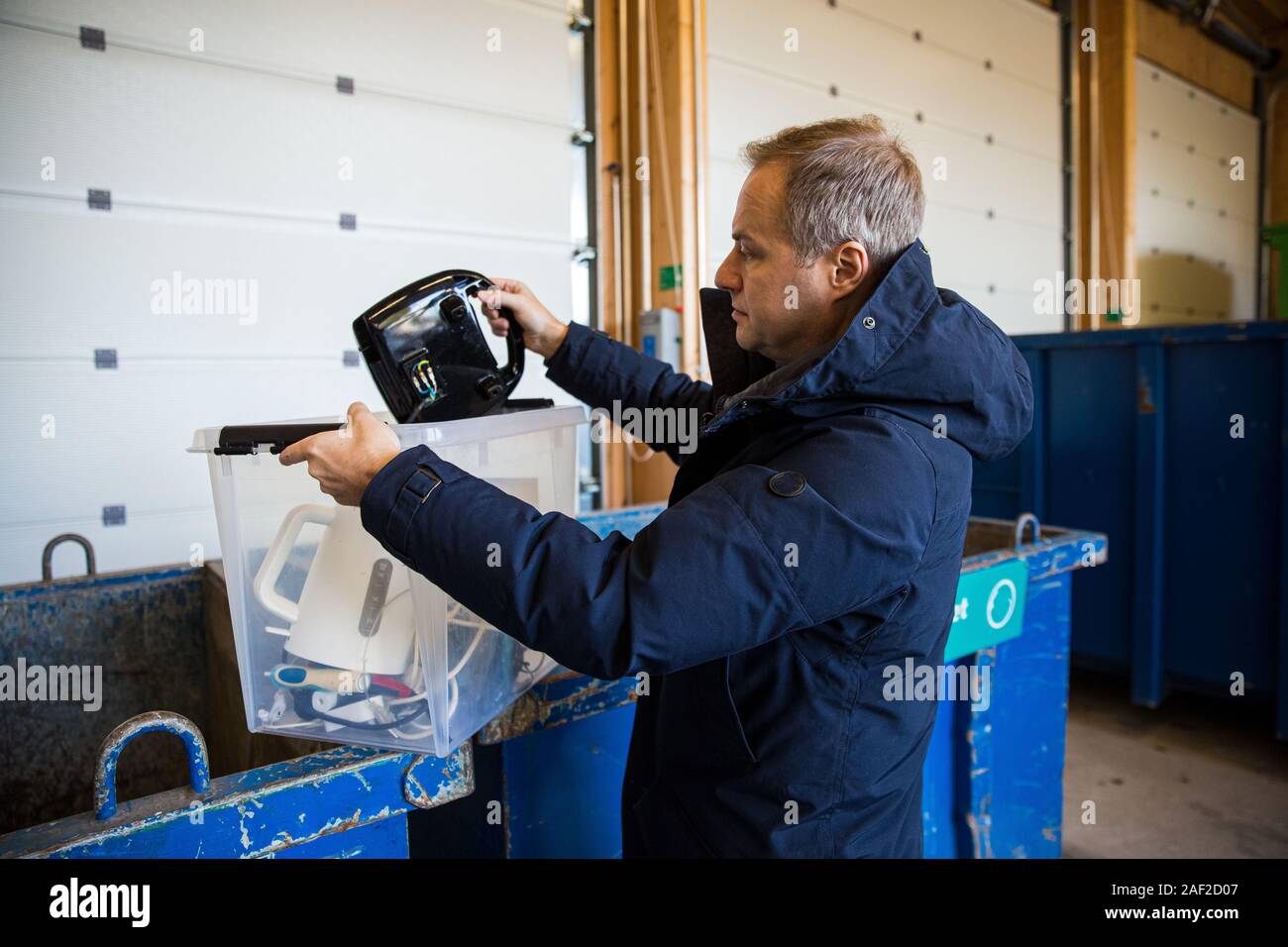 Un hombre poniendo viejos aparatos en el contenedor en el centro de clasificación para la eliminación segura y el reciclaje Foto de stock