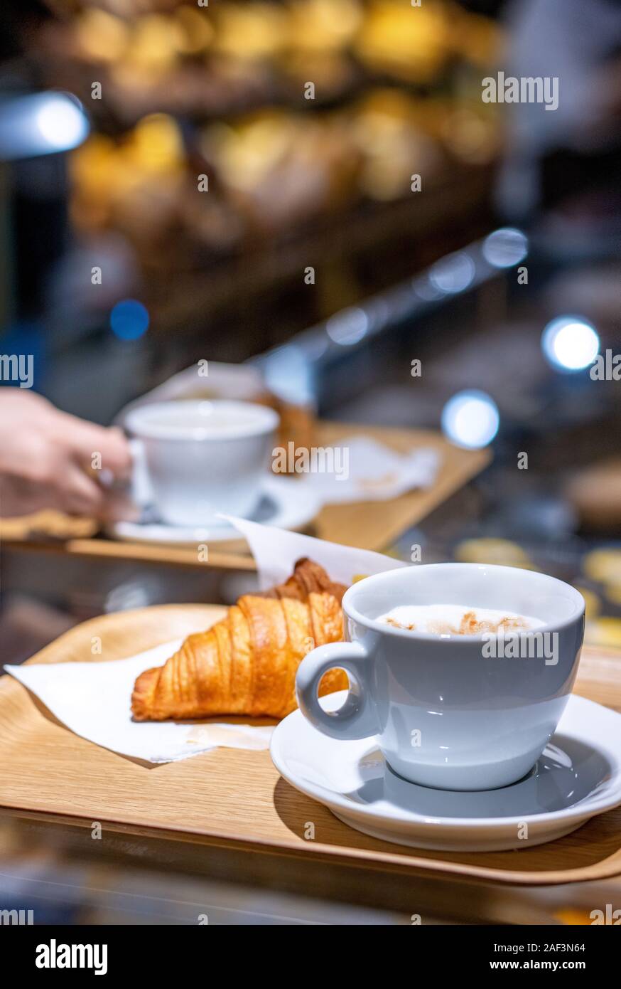 Café y croissant servido en una bandeja en el contador en un borroso fondo de pastelería Foto de stock