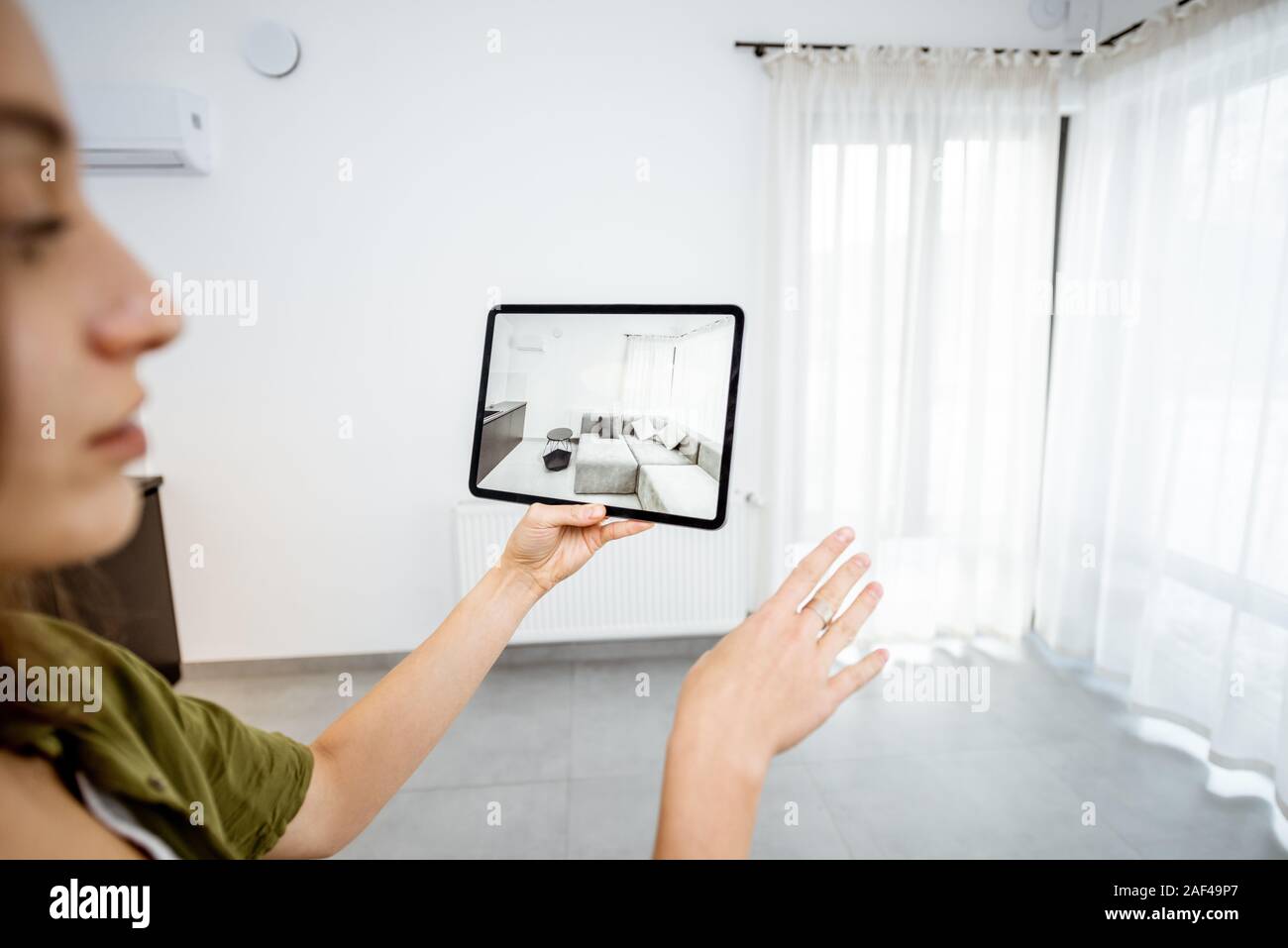 Mujer joven colocar muebles nuevos en una tableta digital en el vacío interior, mirando cómo se ve antes de comprar. Concepto de realidad aumentada en el diseño y retail business Foto de stock