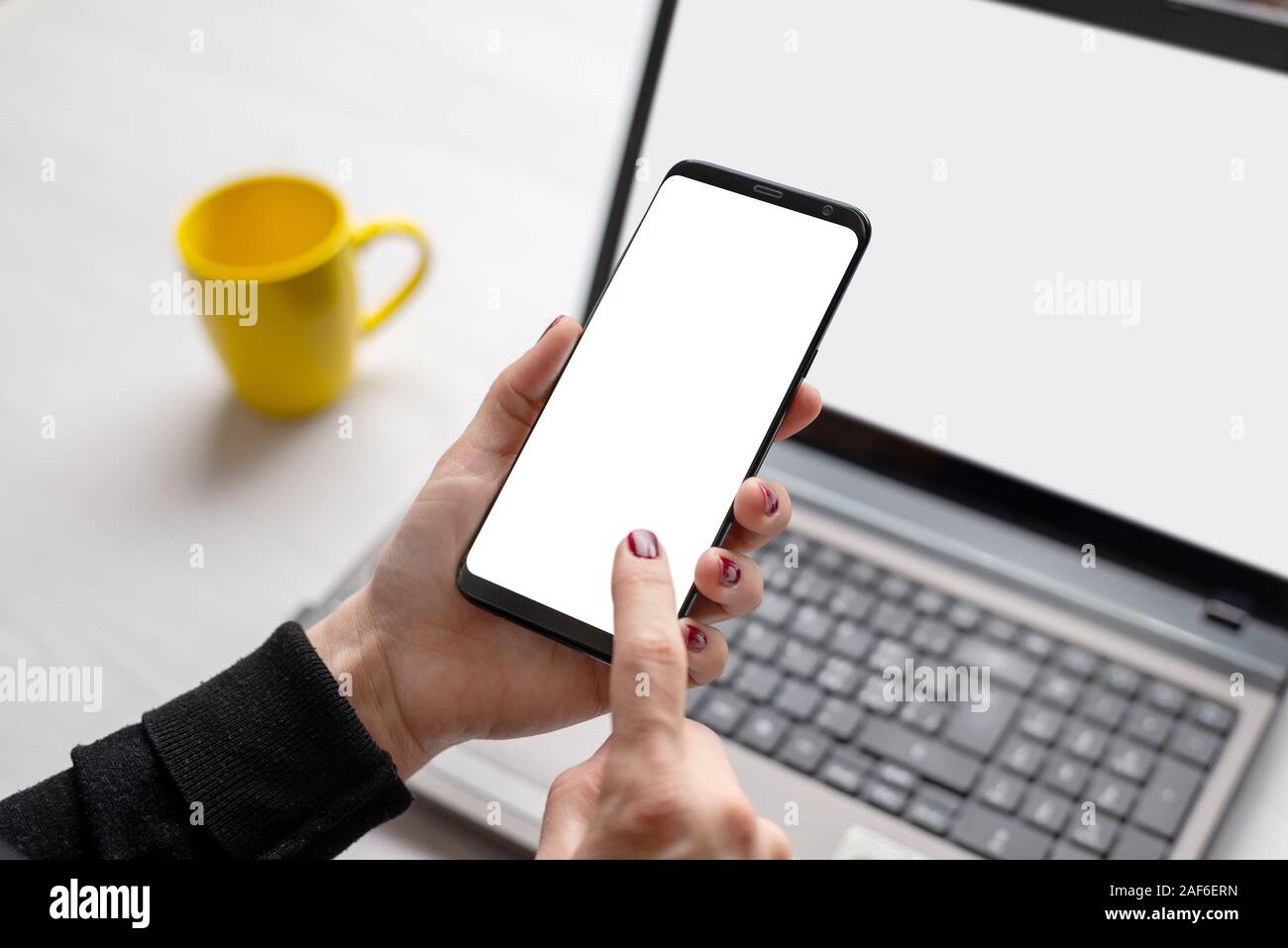 Teléfono con pantalla aislados de boceto en manos de la mujer. Portátil y una taza de café en el fondo. Concepto de trabajo para app o presentación del sitio web Foto de stock
