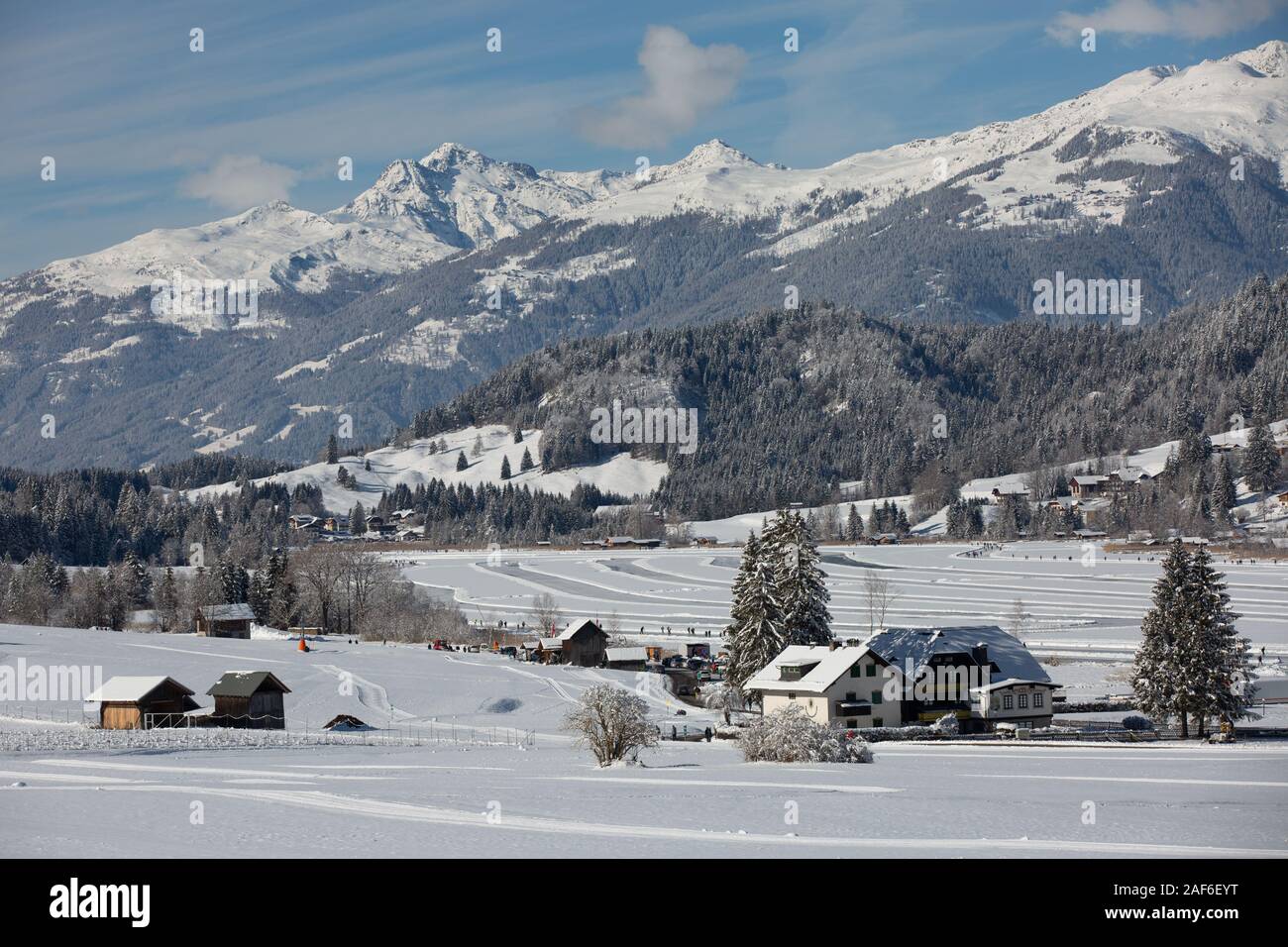 Lago congelado panorama con montañas cubiertas de nieve y bosques. La gente patinar y caminar sobre el lago congelado Weissensee, Carintia, Alpes, Austria Foto de stock