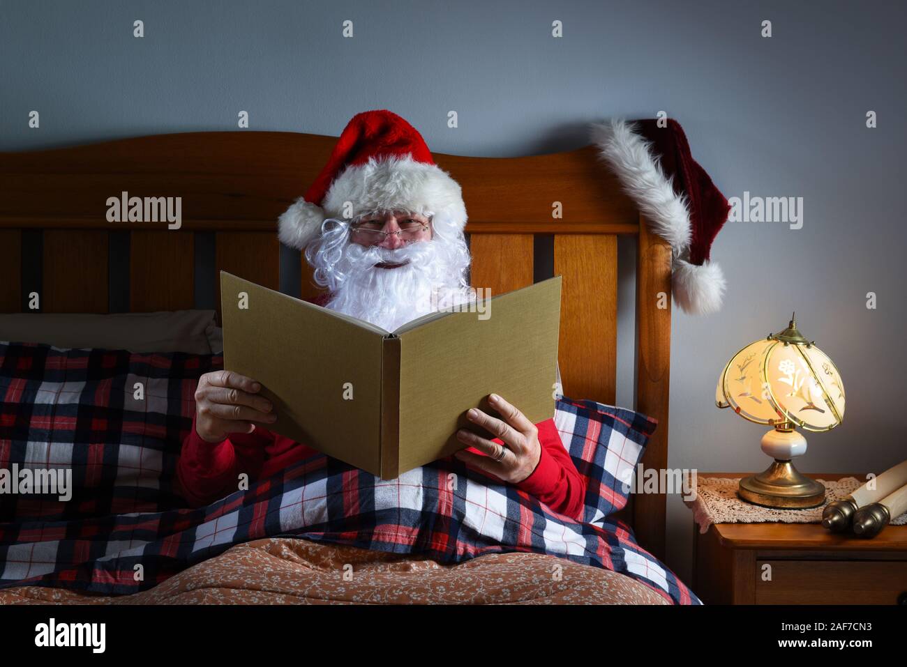 Santa Claus sentado en la cama leyendo un libro grande antes de que él se va a dormir en la víspera de Navidad. Foto de stock
