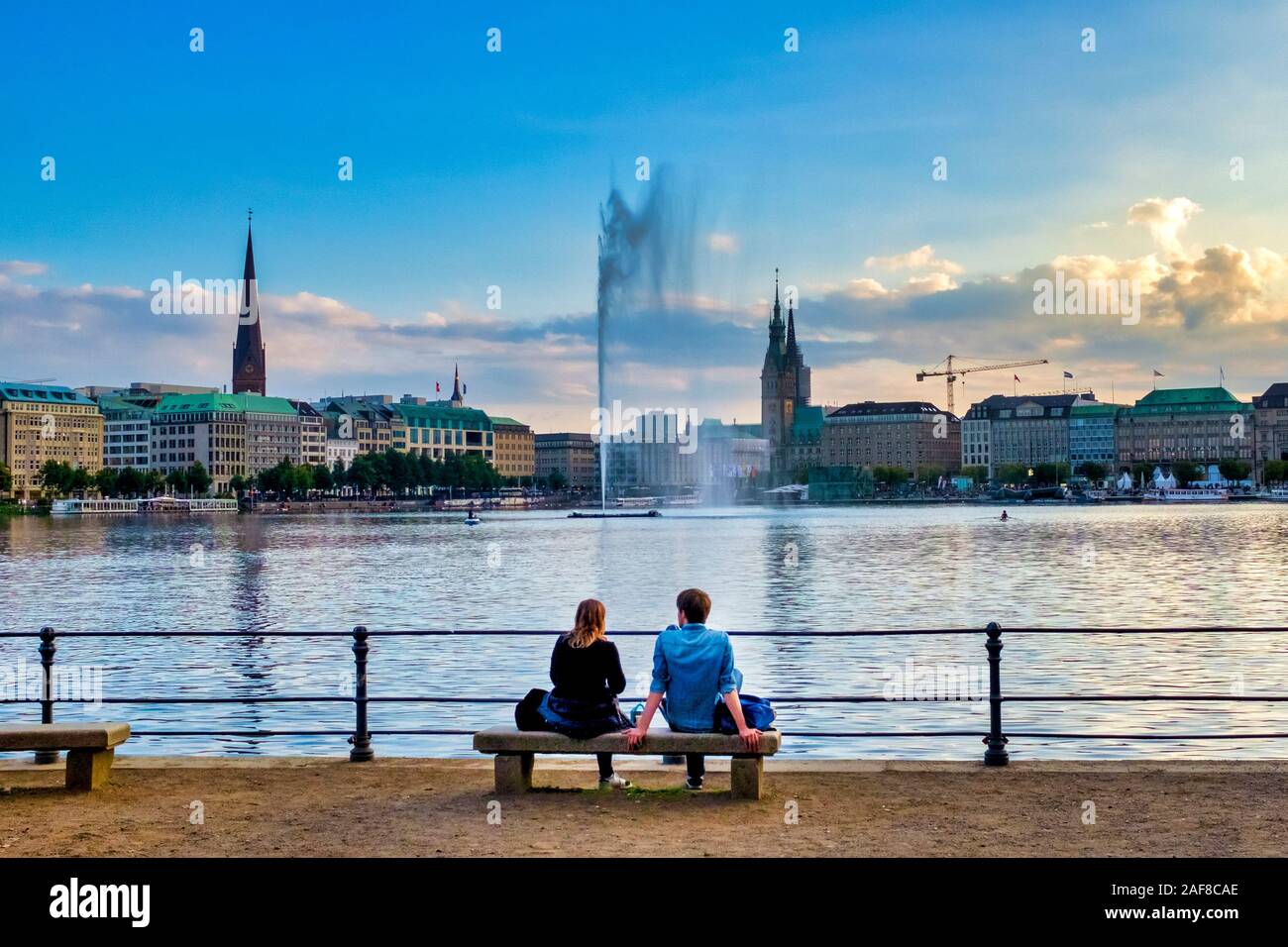 Pareja sentada en un banco en frente del lago Binnenalster (Alster) al atardecer, Hamburgo, Alemania. Foto de stock