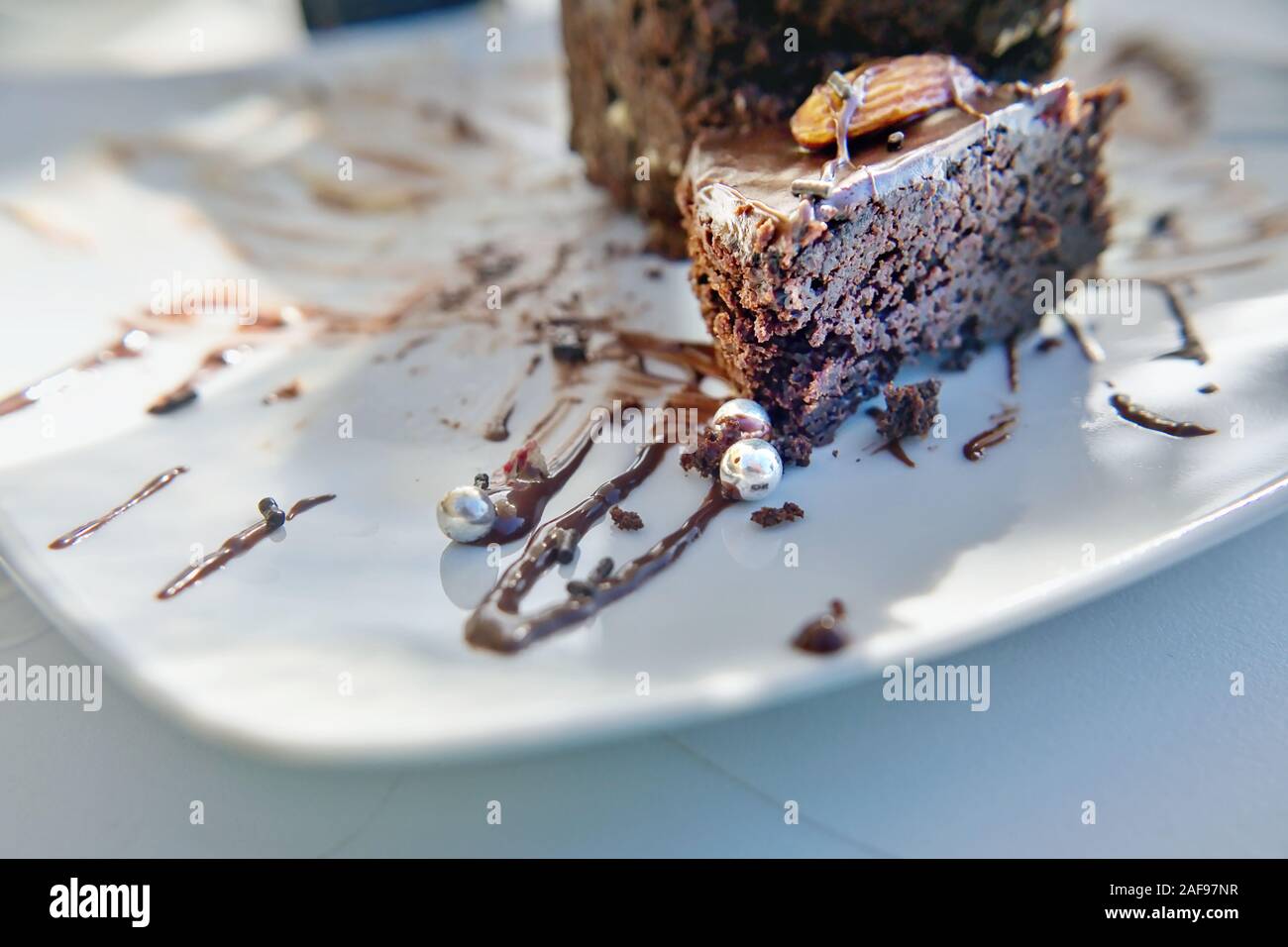 Detalle de una tarta de chocolate con salsa de chocolate, en una placa blanca, el cual está decorado con pequeñas bolas de plata. Cierre con antecedentes muy suave en b Foto de stock