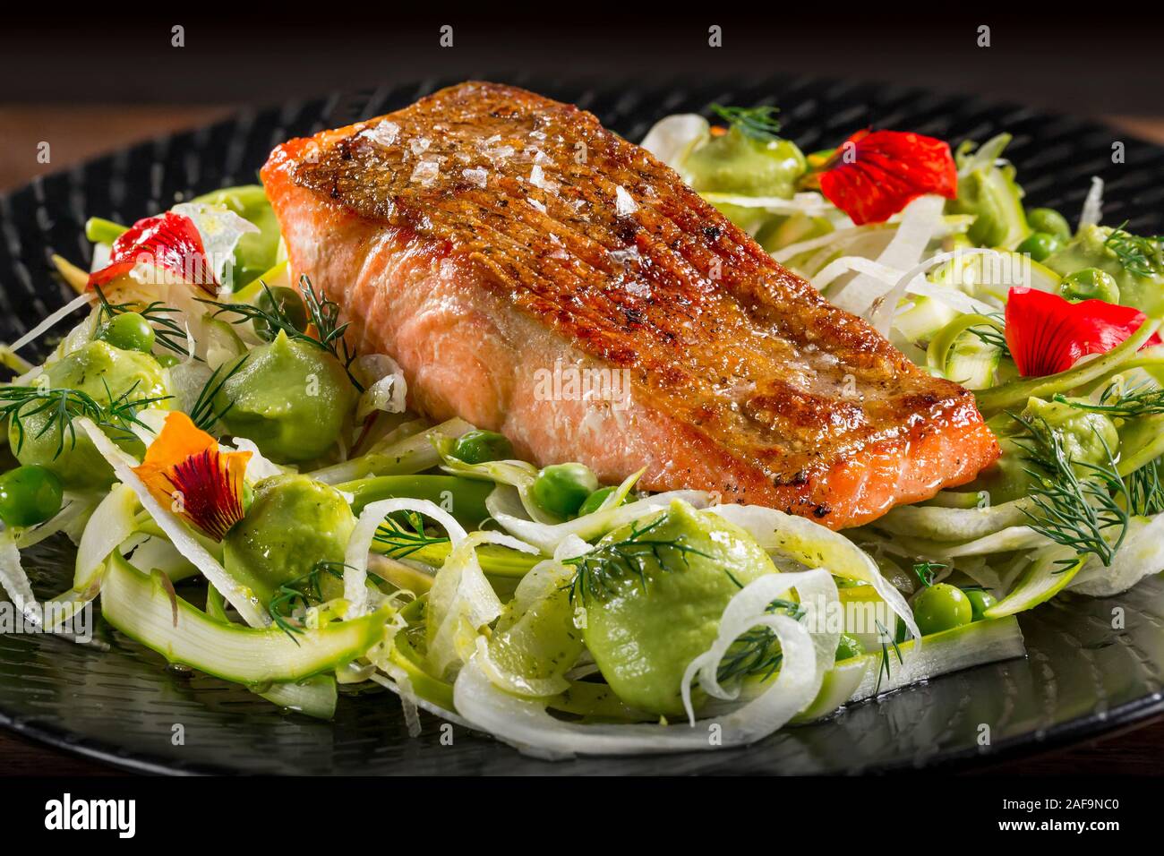 Filete de salmón recién asadas a la parrilla filete de pescado con ensalada de aguacate y fennal sobre una placa negra. Foto de stock