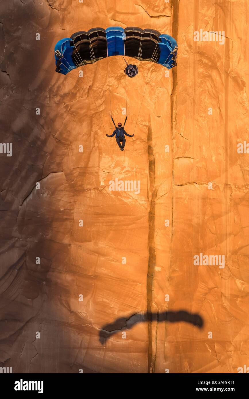 Un puente de base desciende en su paracaídas fuera de la cara vertical de 400 pies de la lápida en Kane Springs Canyon, cerca de Moab, Utah. Nota su sombra en th Foto de stock