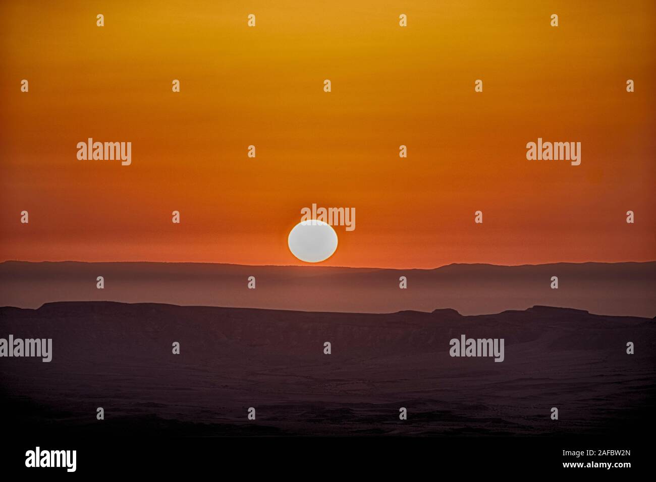 Amanecer sobre el cráter Maktesh Ramon la mañana después de una tormenta de arena se traduce en un color naranja brillante en el cielo. Foto de stock