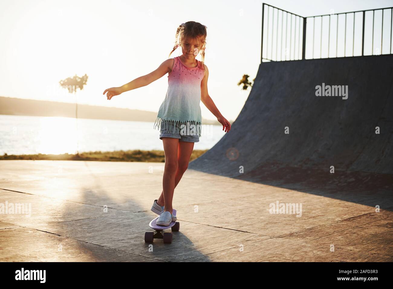 Día soleado. Kid divertirse con el skate en la rampa. Alegre niña Foto de stock