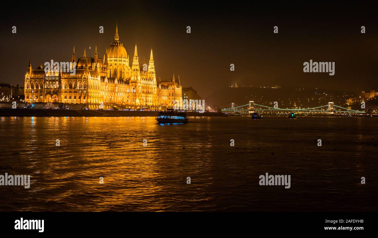 El edificio del Parlamento húngaro en el río Danubio en Budapest, visto desde un barco turístico por la noche Foto de stock