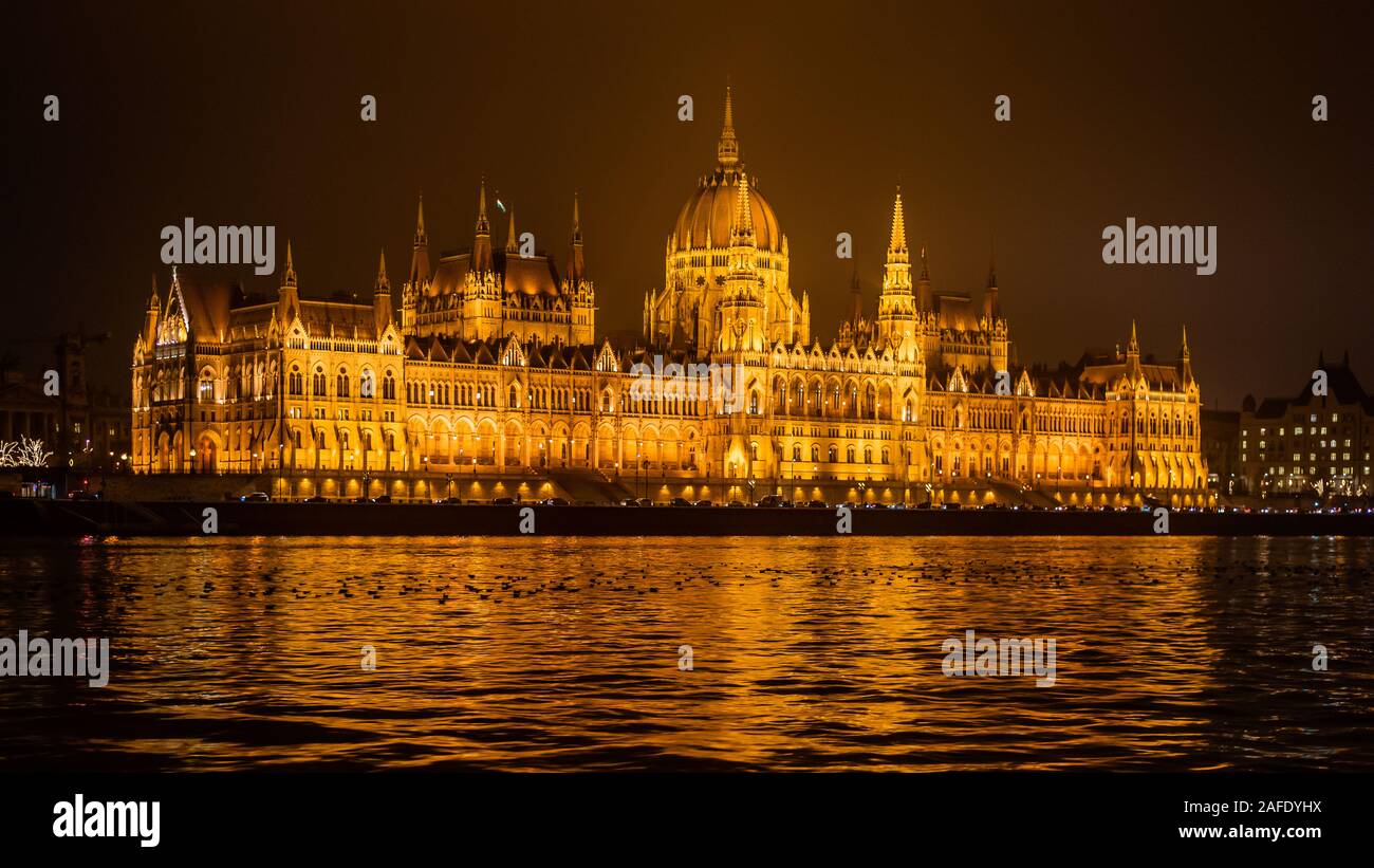 El edificio del Parlamento húngaro en el río Danubio en Budapest, visto desde un barco turístico por la noche Foto de stock