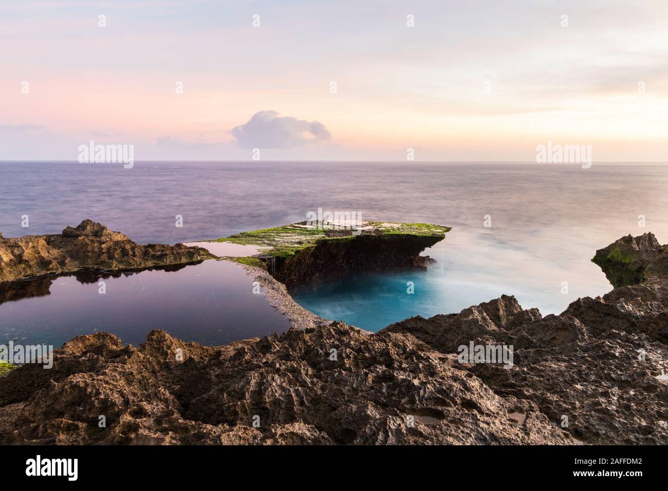 Desgarro del diablo al atardecer, en la isla de Nusa Lembongan, Bali, Indonesia. Costa rocosa en primer plano. Cielo con nubes amarillas más allá. Foto de stock