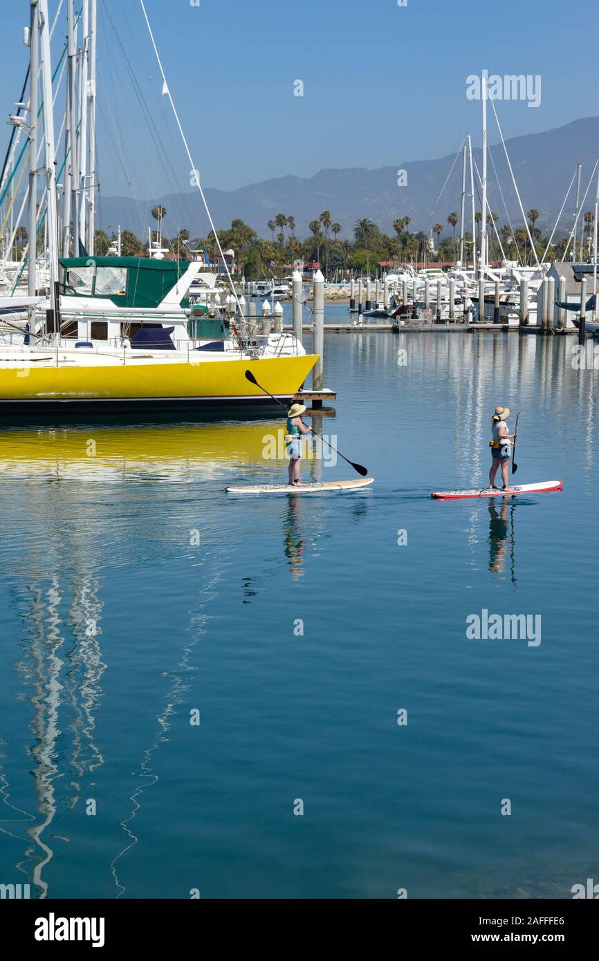 Dos mujeres maniobrar sus Stand Up Paddle juntas a través de un canal cerca de embarcaciones amarradas a la marina en el Puerto de Santa Bárbara, Santa Barbara, CA. Foto de stock