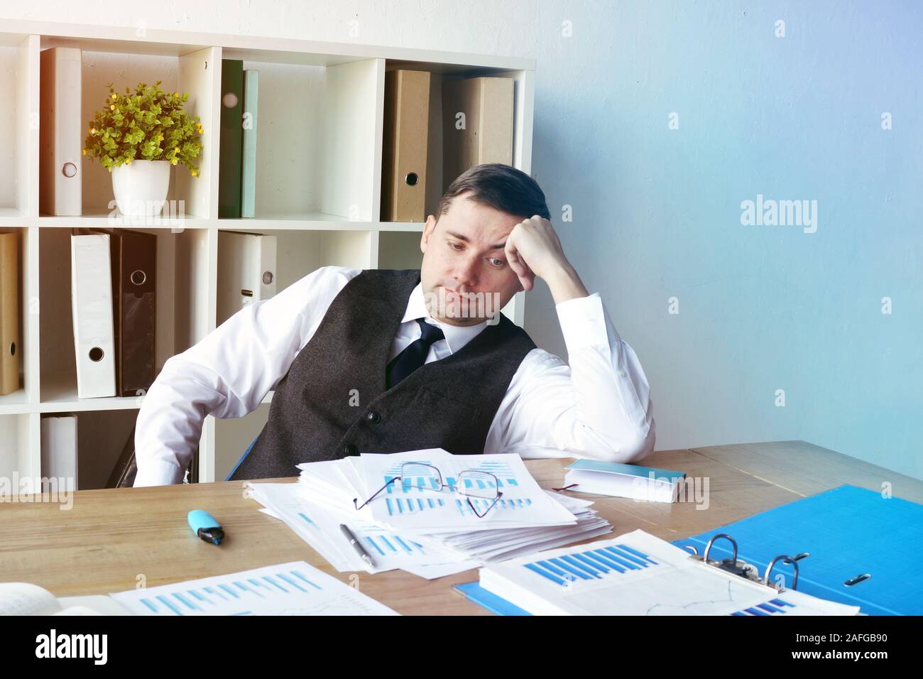 Sobrecargado de trabajo, hombre de negocios con una pila de papeles en el escritorio. Foto de stock
