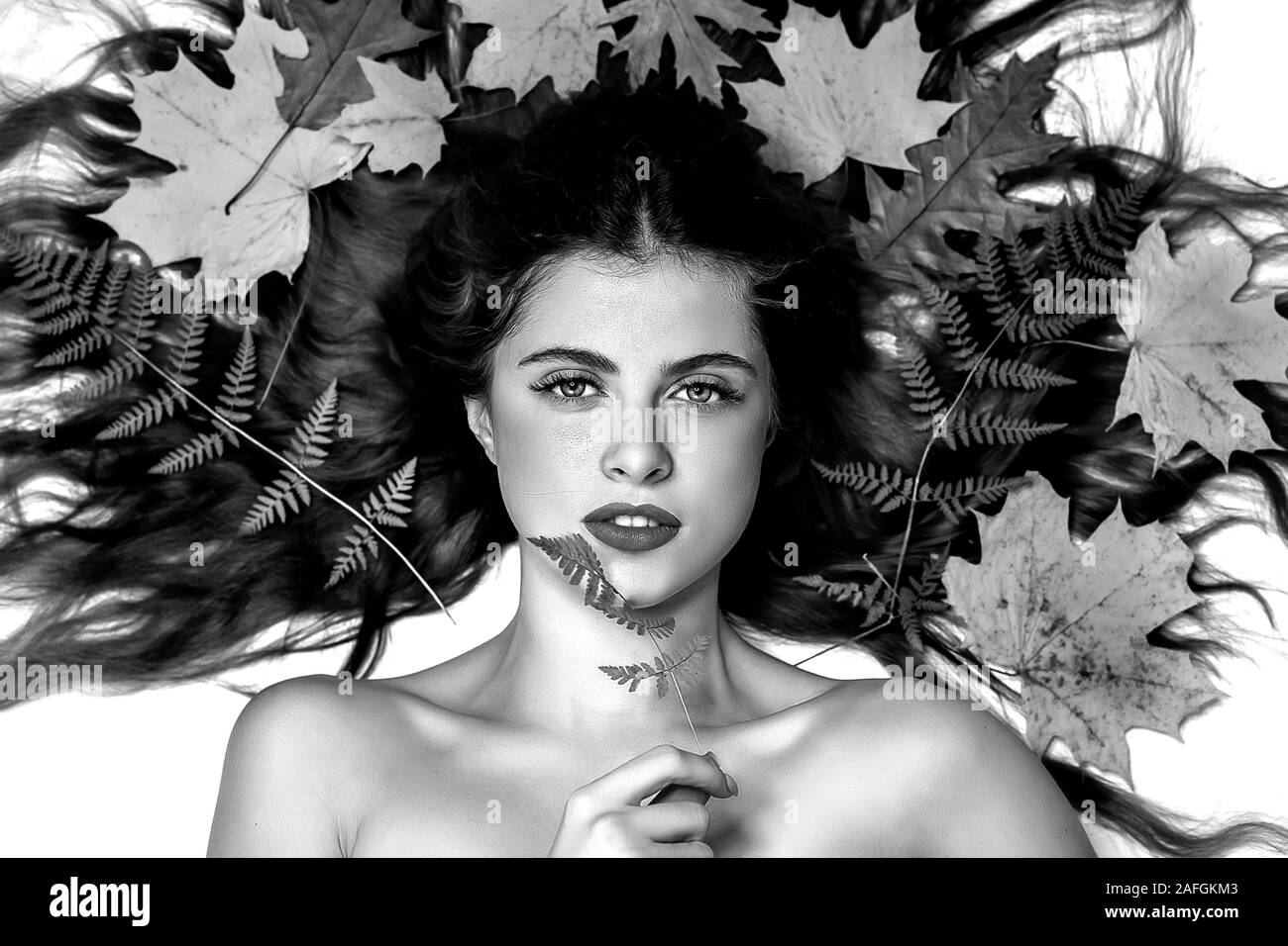 Retrato de una joven mujer morena sobre un fondo blanco con un helecho verde y hojas amarillas alrededor de su cabeza, el cuidado de la piel y el cabello hermoso concepto, SK Foto de stock