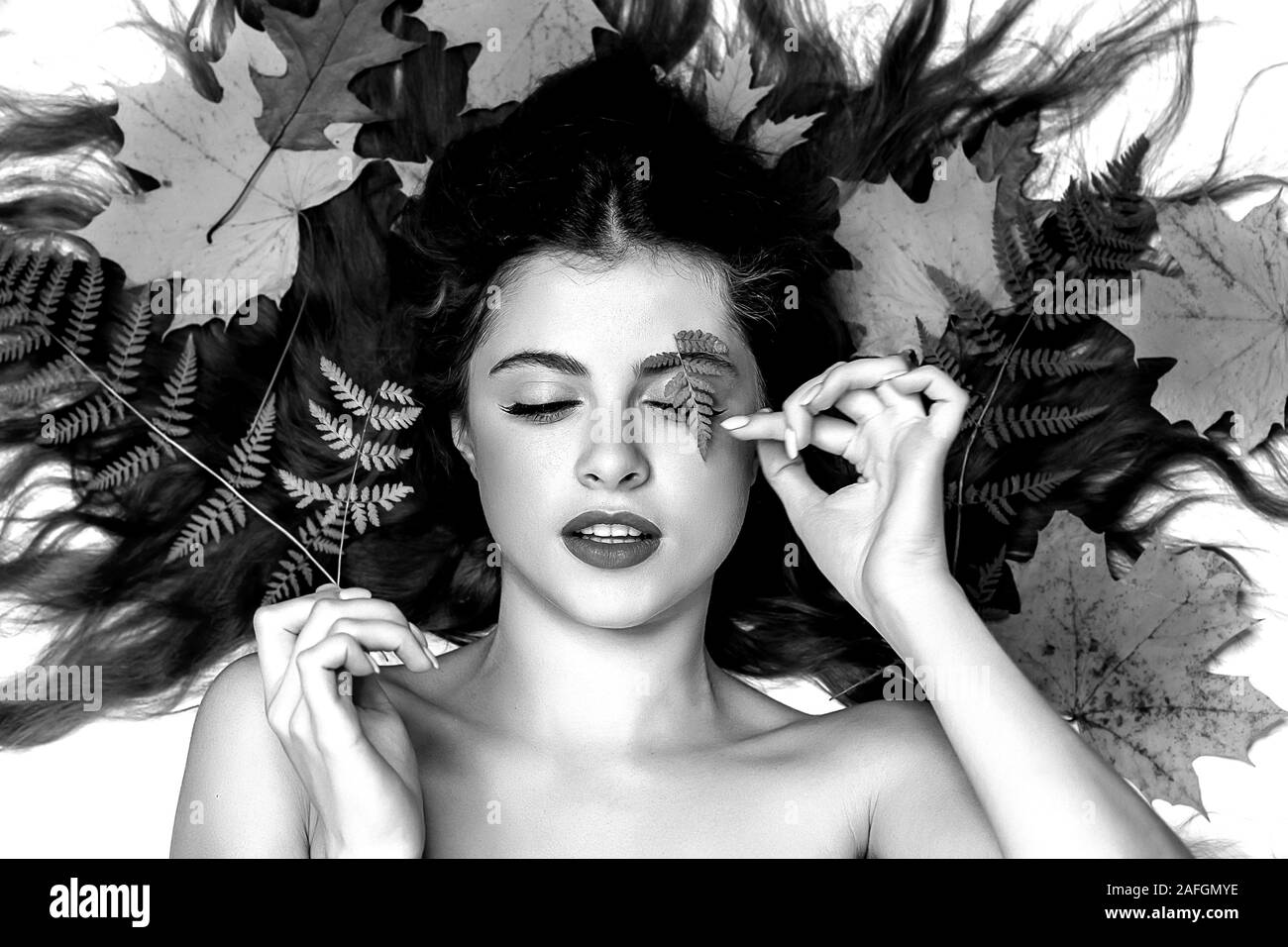 Retrato de una joven mujer morena sobre un fondo blanco con un helecho verde y hojas amarillas alrededor de su cabeza, el cuidado de la piel y el cabello hermoso concepto, SK Foto de stock