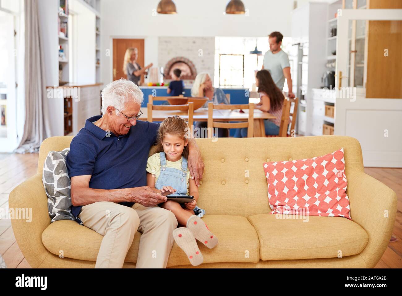 Abuelo sentado con su nieta en el sofá con tableta digital en casa Foto de stock