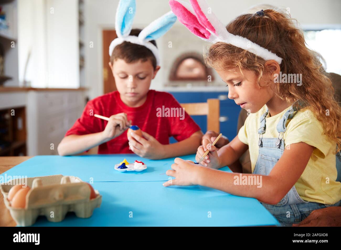 Los niños vestidos de orejas de conejo decorando huevos de Pascua en el hogar Foto de stock