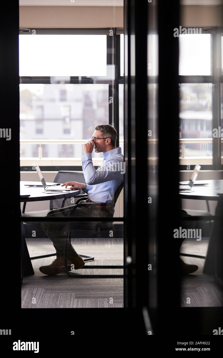 Empresario blanco de mediana edad bebiendo café y trabajar a solas en una sala de reunión, vertical Foto de stock