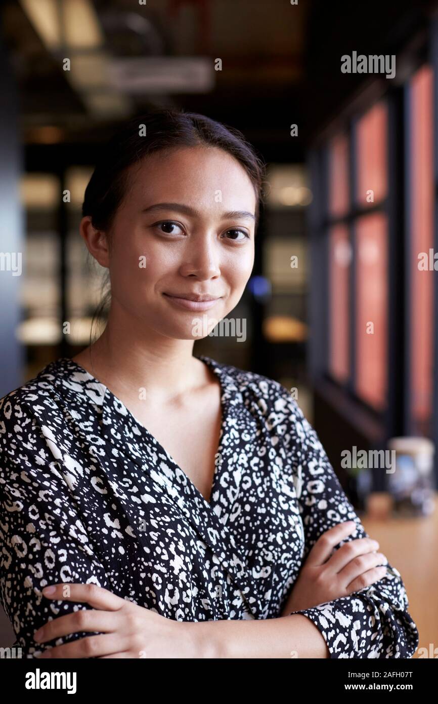 Asia milenaria empresaria por la ventana sonriendo en la oficina a la cámara, de la cintura hacia arriba, vertical Foto de stock