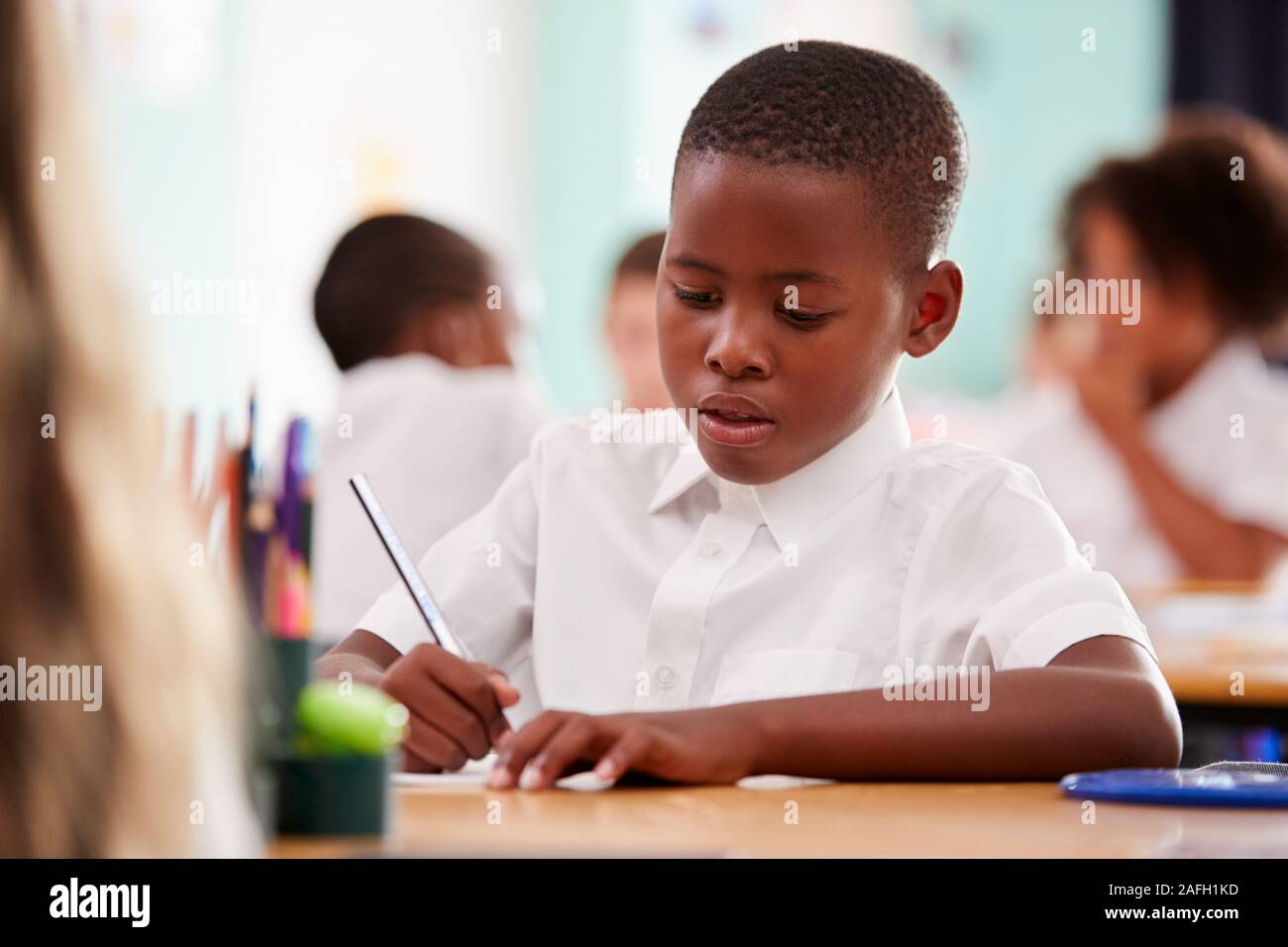 Alumno de la Escuela Elemental de hombres vestidos de uniforme en la mesa de trabajo Foto de stock