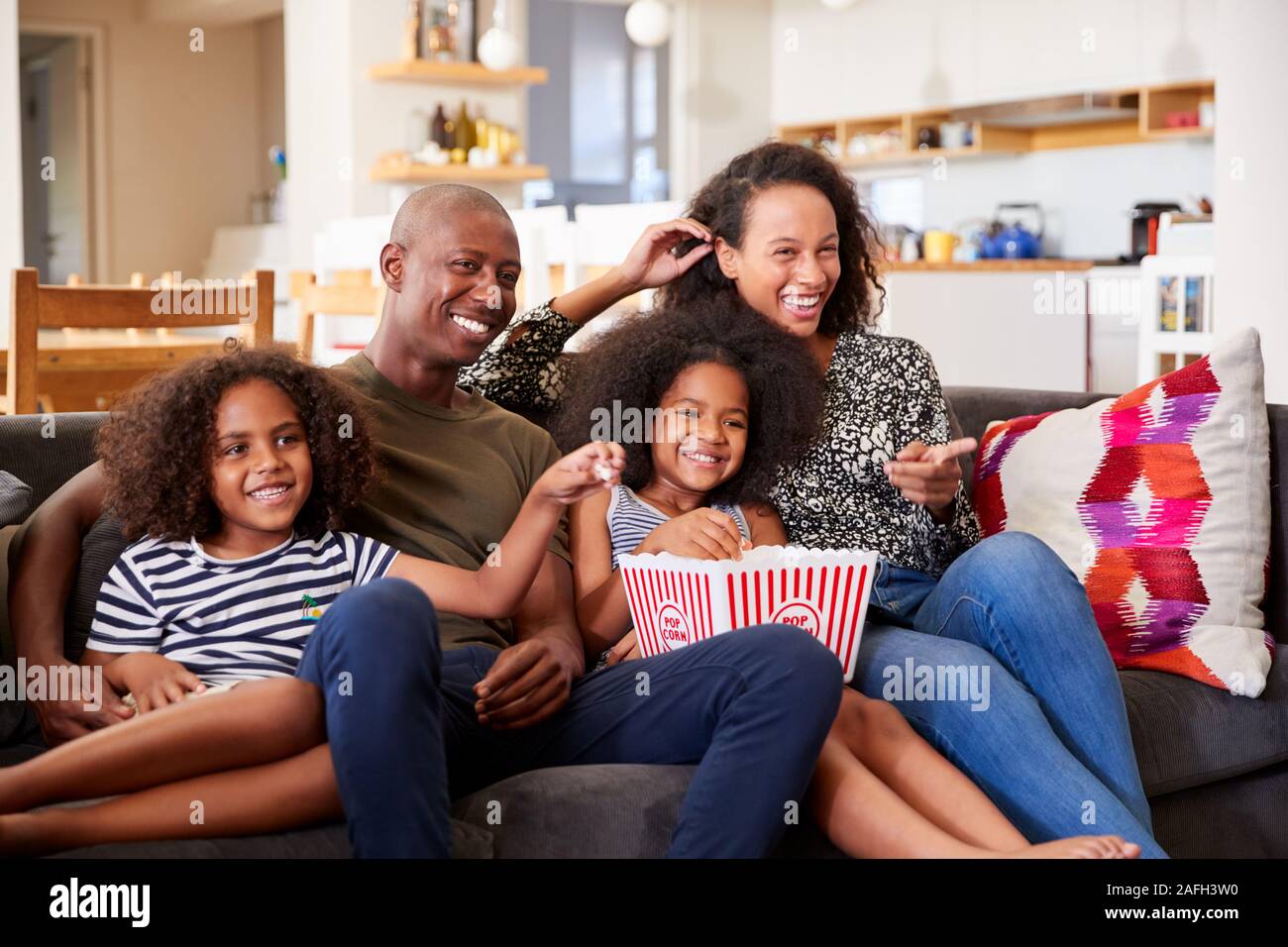 Familia sentada en un sofá en casa comiendo palomitas y viendo la película juntos Foto de stock