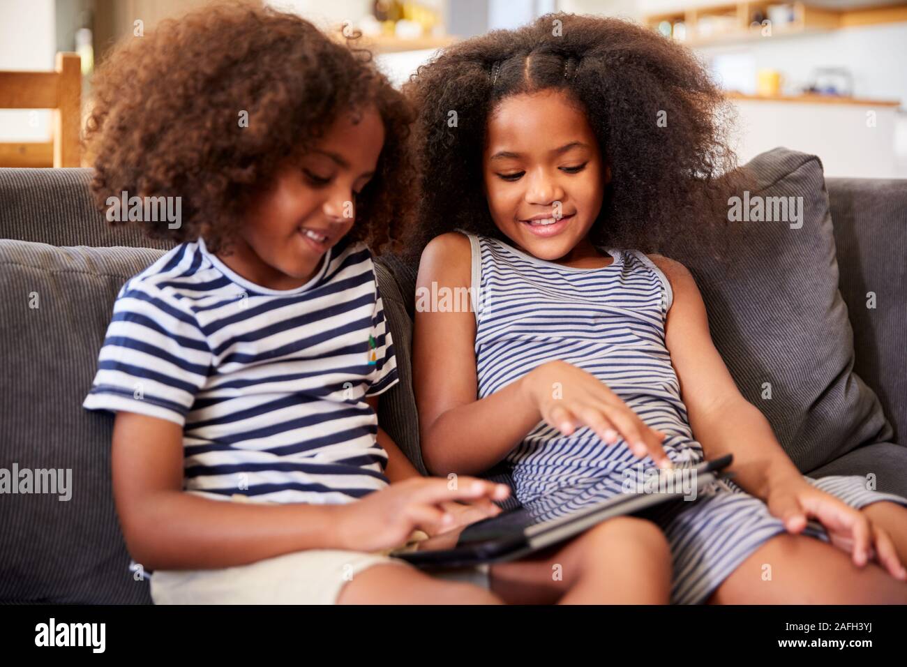 Hermano y hermana, sentada en un sofá en casa jugando con la tableta digital Foto de stock