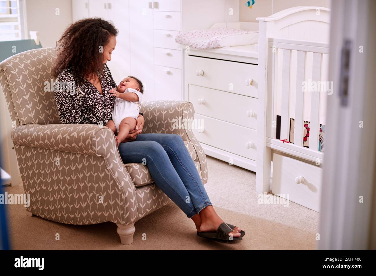 Madre amorosa sentado en la silla abrazando a su Hijo en vivero en casa Foto de stock