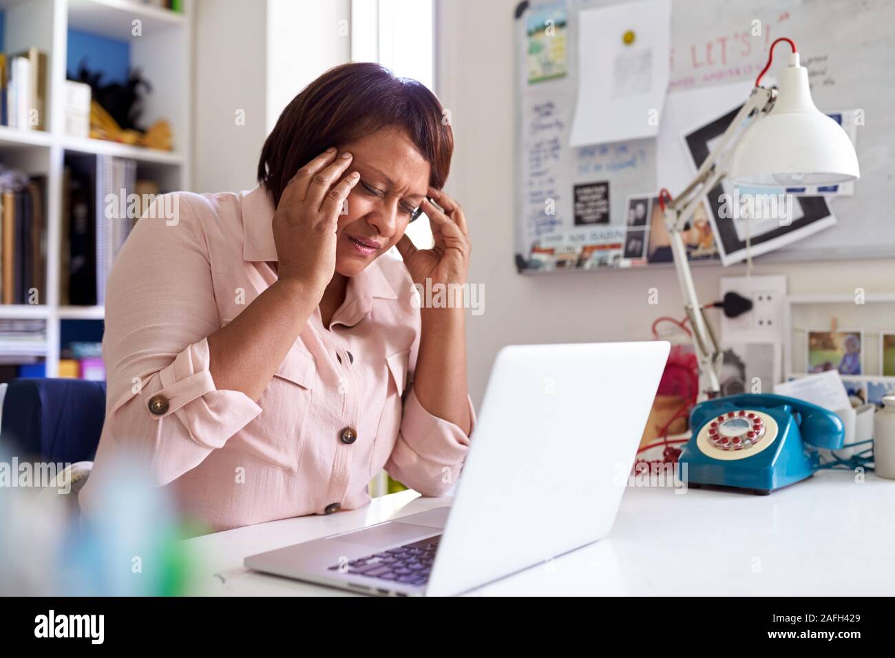 Subrayó mujer madura con portátil trabajando en la oficina en casa Foto de stock