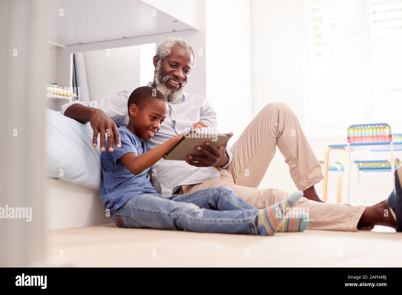 Abuelo sentado con su nieto en Childs Dormitorio utilizando Tablet Digital juntos Foto de stock