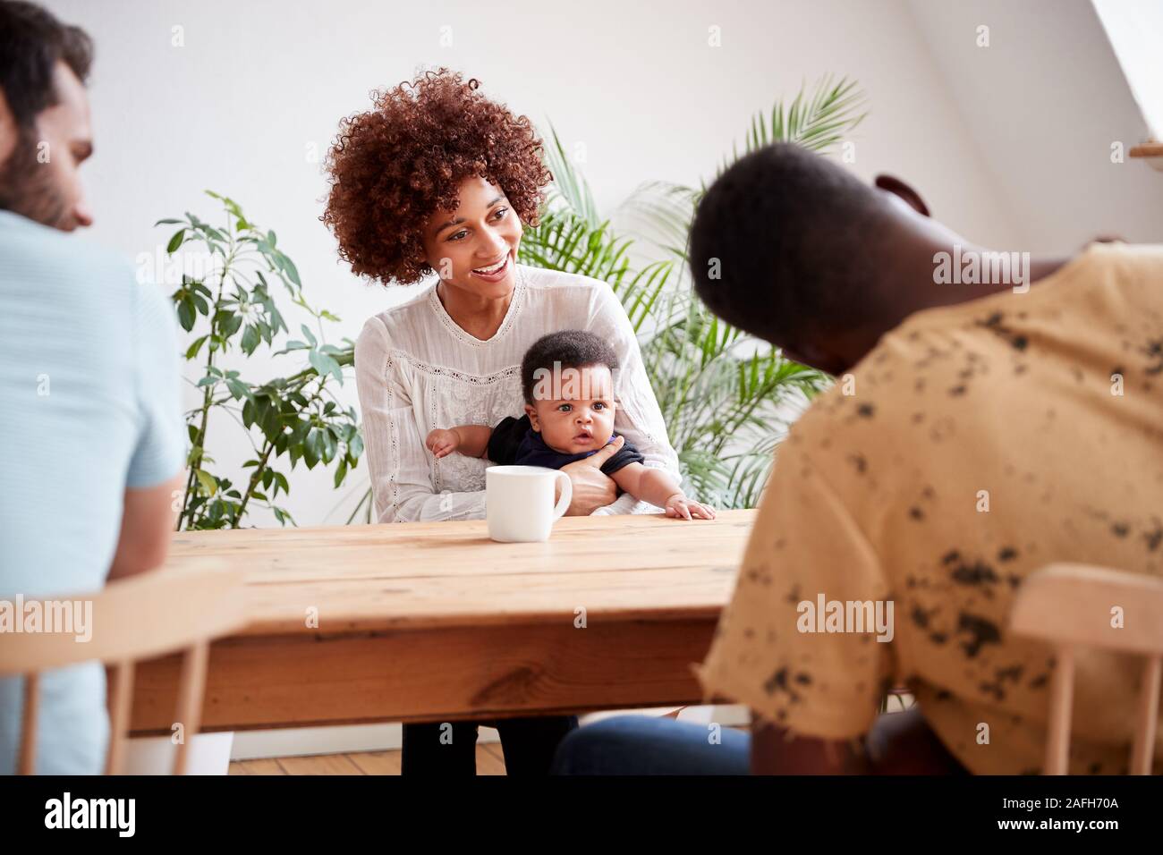 Dos familias con bebés reunirse y conversar en torno a una mesa a jugar la fecha en casa Foto de stock