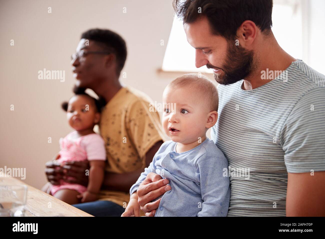 Dos familias con bebés reunirse y conversar en torno a una mesa a jugar Fecha Foto de stock