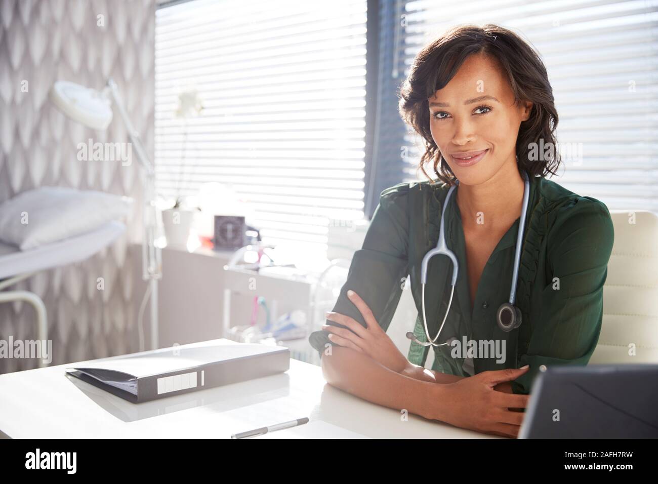 Retrato de mujer sonriente doctor con estetoscopio sentado detrás de escritorio de oficina Foto de stock