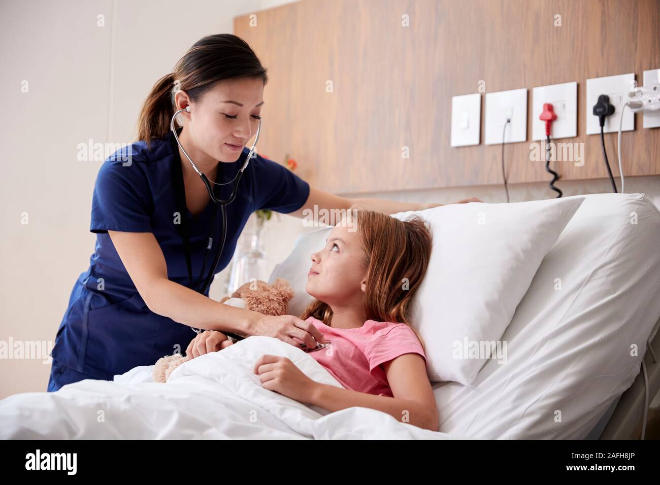 Enfermera examinando chica acostado en la cama del hospital abrazando a Teddy Bear Foto de stock