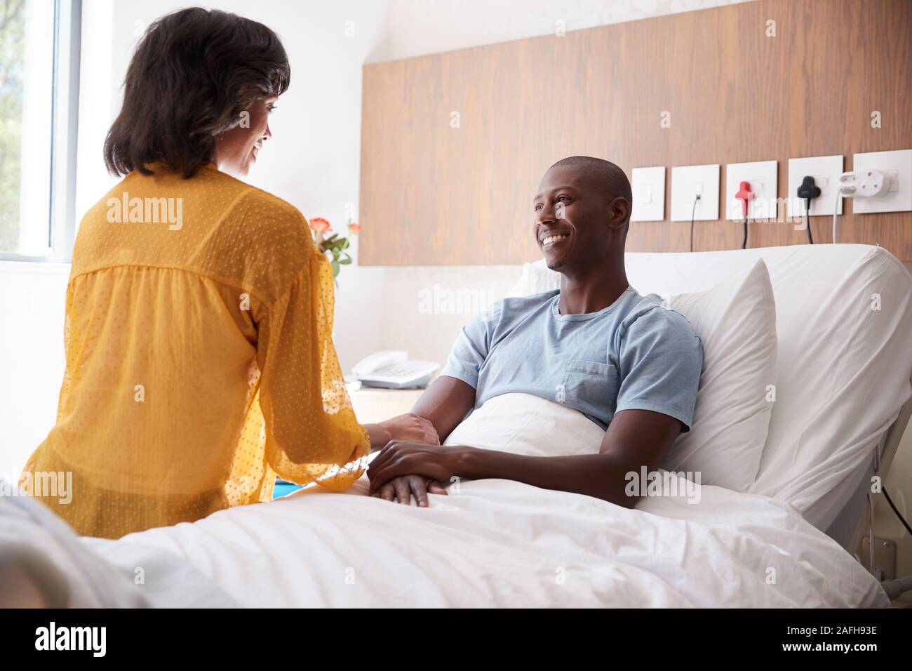 Esposa visitando y hablando con el marido en la cama de un hospital del paciente Foto de stock