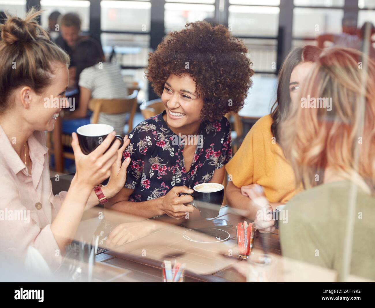 Cuatro amigas jóvenes reunión sentarse en la mesa de café y hablar Foto de stock