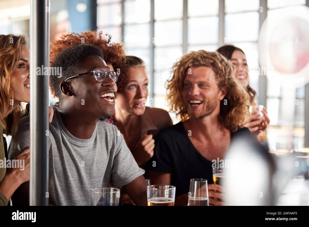 Grupo de Amigos masculinos y femeninos celebrando mientras estás viendo en la pantalla de juego en el bar de deportes Foto de stock