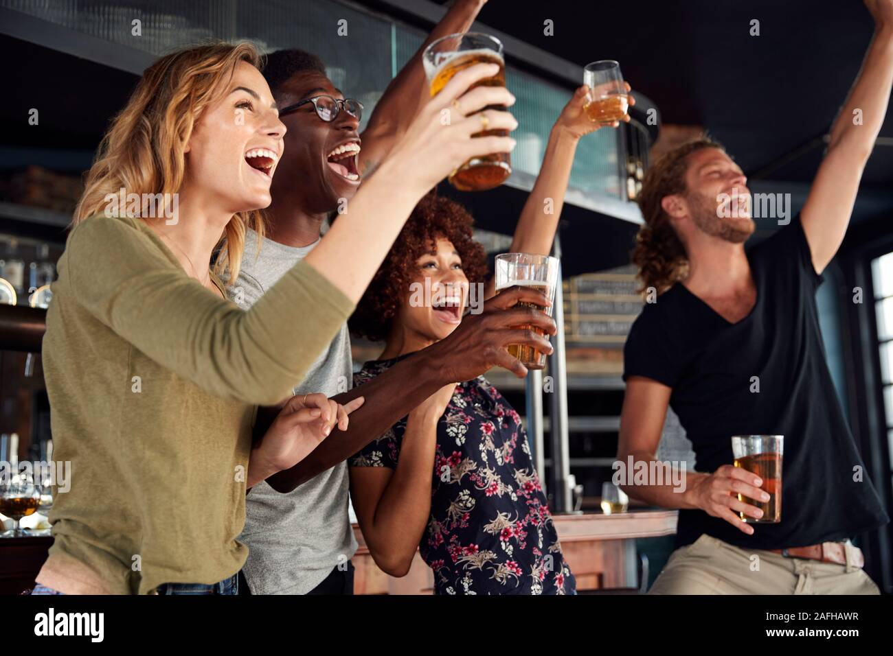 Grupo de Amigos masculinos y femeninos celebrando mientras estás viendo en la pantalla de juego en el bar de deportes Foto de stock