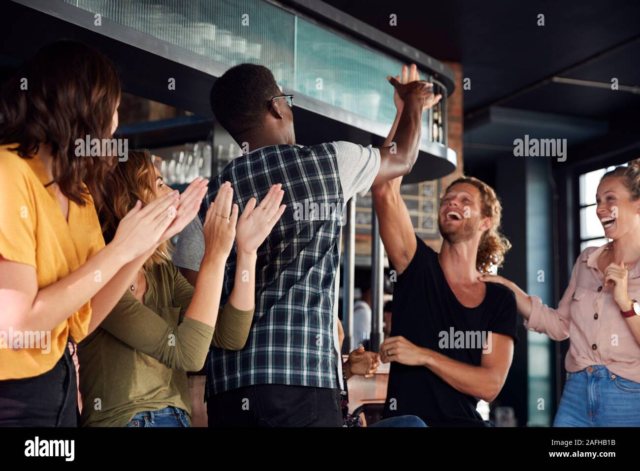 Grupo de Amigos masculinos y femeninos celebrando mientras estás viendo en la pantalla de juego en el bar de deportes Foto de stock