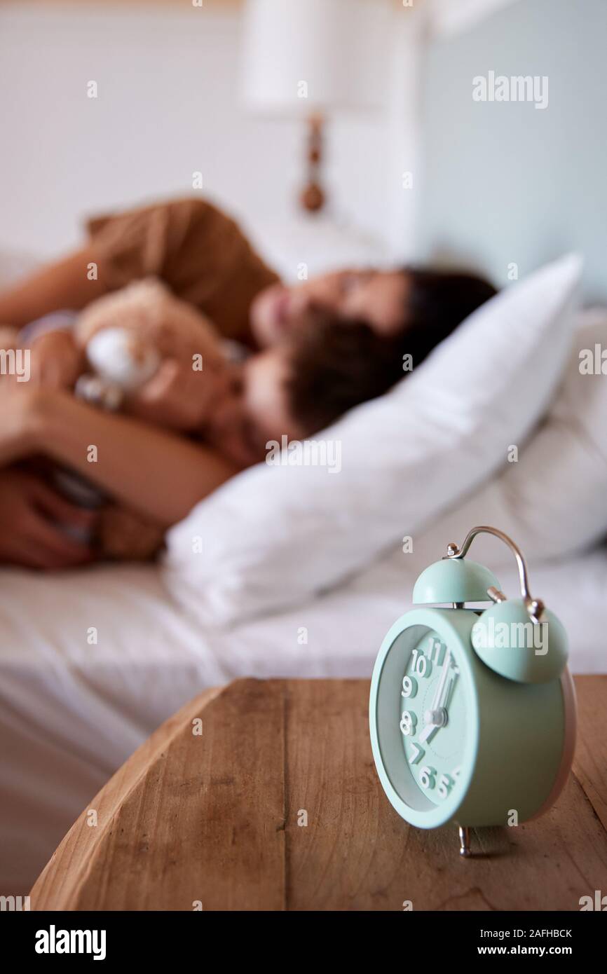 Mujer adulta media durmiendo en la cama con su hijo de cuatro anos, se centran en el despertador en primer plano Foto de stock